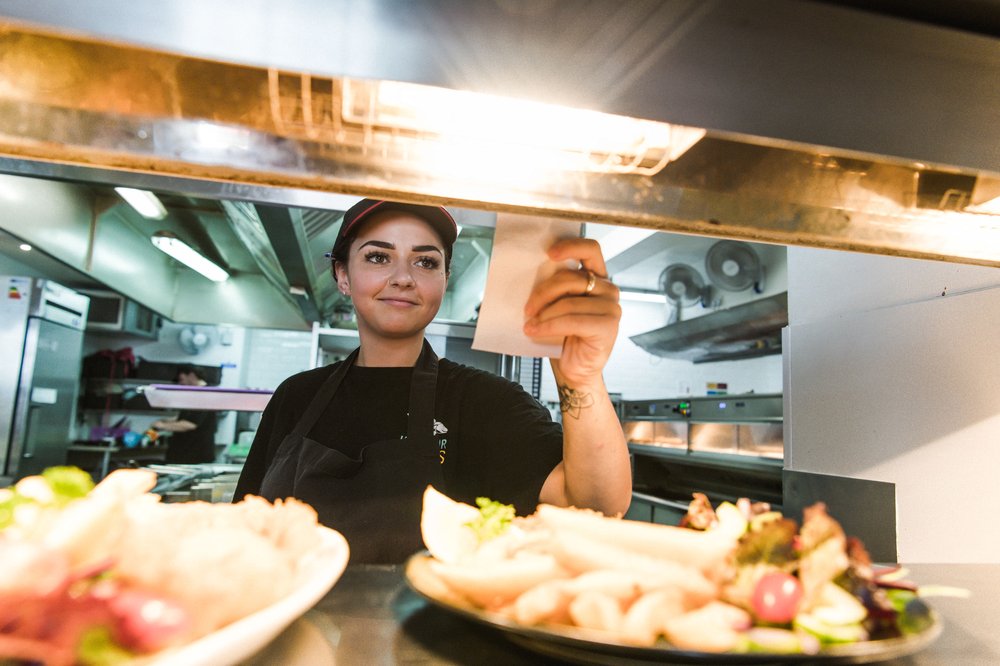 A female kitchen worker in a black uniform reads an order